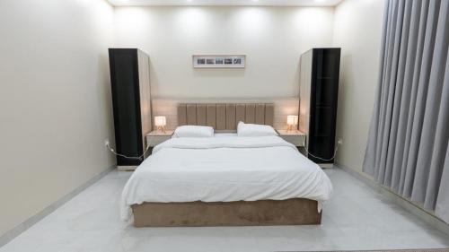 a bedroom with two beds with white sheets and two lamps at Cozy Escape in Dammam