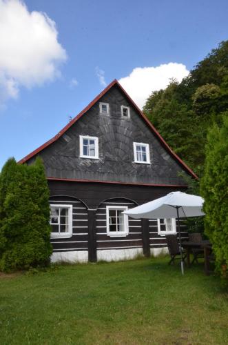 a black house with a table and an umbrella at Penzion U kozy in Chřibská