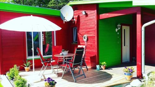 a red and green house with a table and chairs and an umbrella at Ferienwohnung am Malchiner See mit Boot und Kanu in Seedorf