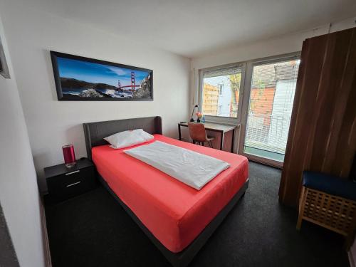 Schlafzimmer mit einem roten Bett, einem Schreibtisch und einem Fenster in der Unterkunft Gästehaus Schröder in Groß-Gerau
