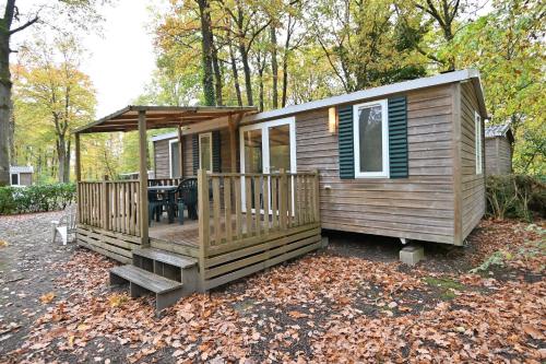 a wooden cabin with a deck in the woods at La Clairière Clim Terrasse BBQ in Mirgaudon
