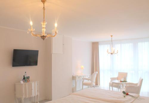 a white room with a bed and a table and a chandelier at Hotel Brenner in Koblenz