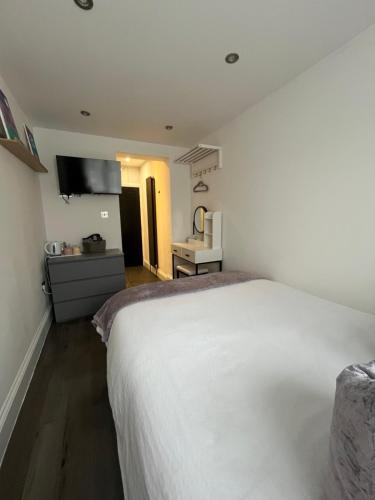 a bedroom with a white bed and a kitchen at Double Guest Room 40 minutes from Central London in Chessington