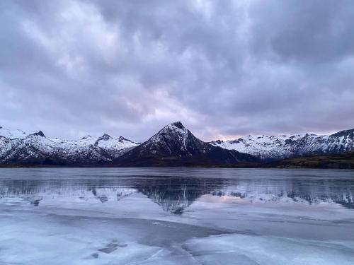 a snow covered mountain range with a reflection in a lake at Charming cabin by the sea in Lofoten in Sandsletta