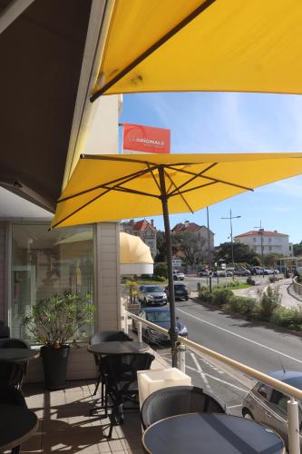 鲁瓦扬Hôtel The Originals Miramar, Royan Pontaillac的天井上的黄色遮阳伞,配有桌椅