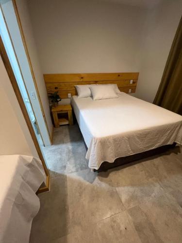 a bedroom with a white bed with a wooden headboard at Suíte no Rancho Minas in Porto Seguro