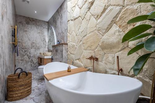 ein Badezimmer mit einer weißen Badewanne und einer Steinmauer in der Unterkunft Villa Marcel Premium by Tofino Villas in Uluwatu