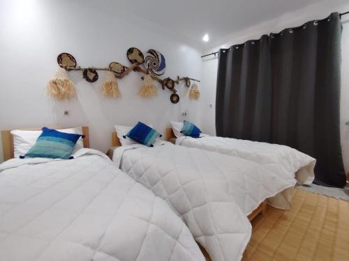 a bedroom with two beds with white sheets and blue pillows at Mira bay surf house in Imsouane