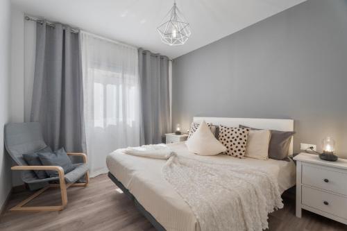 een witte slaapkamer met een bed en een stoel bij 4 Apartamentos Omanai Tenerife Sur in Las Galletas