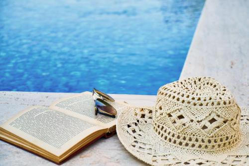 a straw hat and a book next to a swimming pool at Sercotel Barcelona El Prat in El Prat de Llobregat