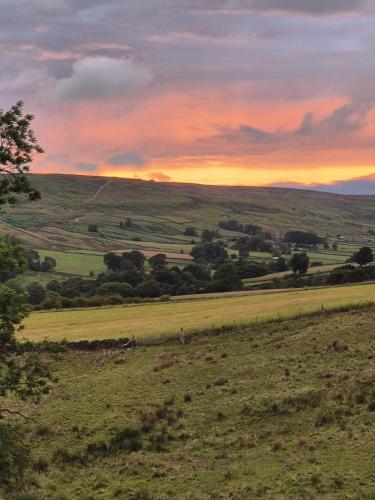 a view of a field with a sunset in the background at Craven Garth Cottages in Rosedale Abbey