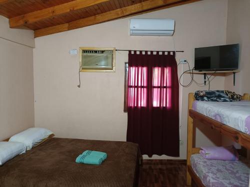 a room with two beds and a window with a red curtain at Hostel el Amanecer in Puerto Iguazú