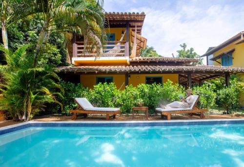 een man zittend op een stoel naast een huis met een zwembad bij Pousada Sabina in Barra Grande