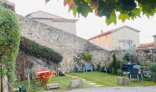 a garden outside a stone wall with chairs and tables at Les Rêves D'Eglantine, maison d'hôtes in Saint-Cyr