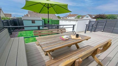 Un banco de madera sentado en una terraza con una sombrilla. en Sandbanks Braunton, Stylish Cottage near to Saunton Beach Sleeps 4, en Croyde
