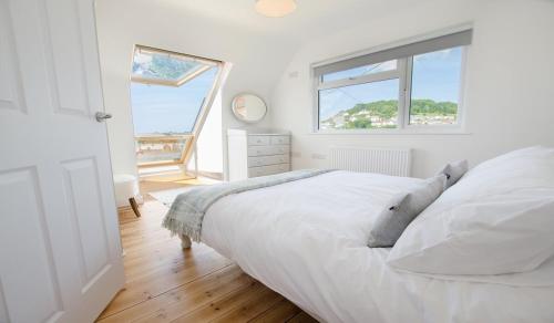 een witte slaapkamer met een bed en een raam bij Rooftops Braunton, Stylish Beach House - Fantastic Views - Hot Tub hire - Sleeps 8 in Braunton