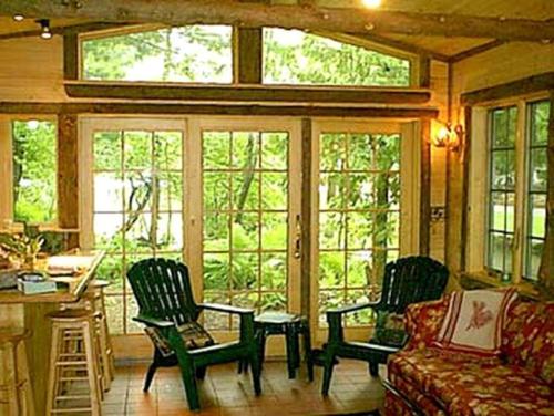 een woonkamer met een bank, stoelen en ramen bij All Season Romantic One-Room Cabin on Moody Pond, in Upstate New York in Saranac Lake
