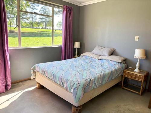 a bedroom with a bed with purple curtains and a window at Field's End in Howick