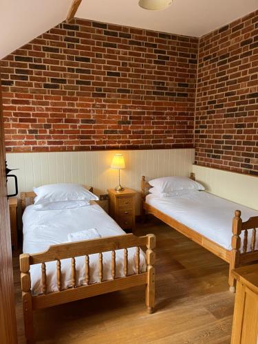 two beds in a room with a brick wall at Blashford Manor Farmhouse Holiday Cottage - The Shire Cottage in Ellingham
