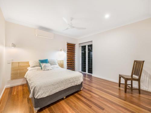 a white bedroom with a bed and a chair at 3 Moffat Beach Holiday House in Caloundra