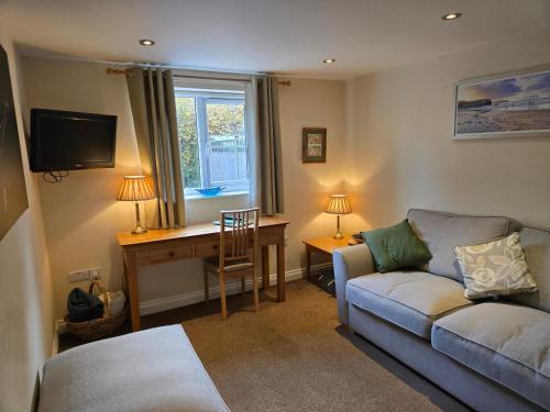 a living room with a couch and a desk and a window at Farthing Cottage in Norwich