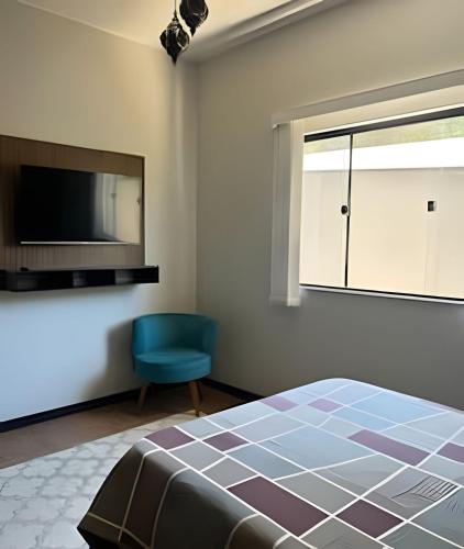 a bedroom with a bed and a tv and a blue chair at Flat Funcional Moderno | Conforto e Praticidade in Nova Friburgo