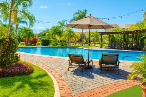 a patio with two chairs and an umbrella next to a pool at Family Home close to the Beach, Vidanta, Aqua Adventures with Pool & Parking in Nuevo Vallarta