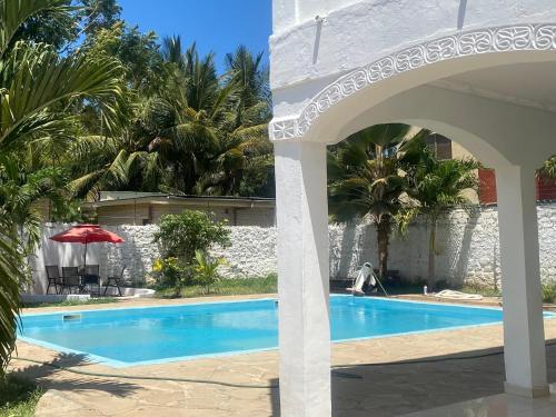 uma piscina com um guarda-sol vermelho e palmeiras em Upendocozy villa em Praia de Diani