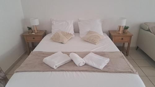 a white bed with three pillows on it with two tables at Rêve Créole, accès piscine, plage et golf in Saint-François