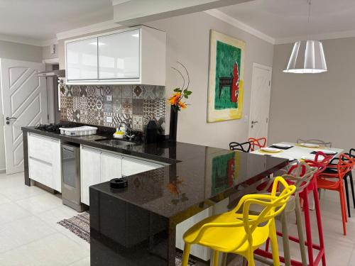 a kitchen with a black counter and yellow chairs at Apartamento completo, 200mts da praia de Pitangueiras in Guarujá