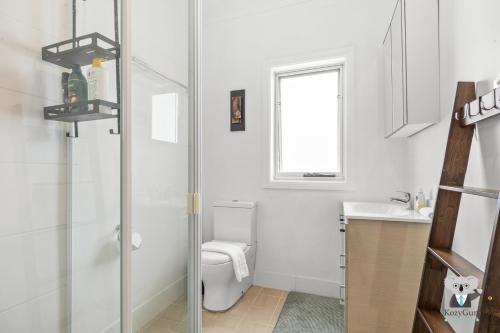 Un baño blanco con inodoro y lavabo. en KozyGuru | Erina | Sunny Coastal Escape + Parking, en Erina East
