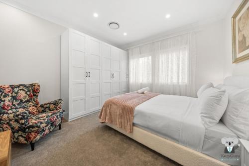 Un dormitorio blanco con una cama y una silla. en KozyGuru | Erina | Sunny Coastal Escape + Parking, en Erina East