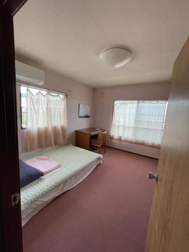 a bedroom with a bed and a desk and windows at kumanonisumu! in Kumano