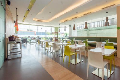 a restaurant with white tables and yellow chairs at Zest Jemursari by Swiss-Belhotel International in Surabaya