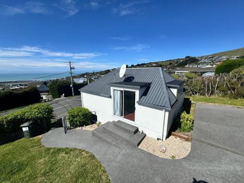 a small white house with a black roof at Belleview Cottage- Cute cottage with views of sea, city and snowpeeks in Christchurch