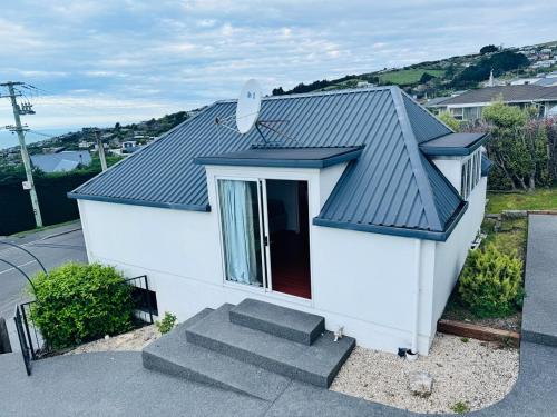a small white house with a black roof at Belleview Cottage- Cute cottage with views of sea, city and snowpeeks in Christchurch
