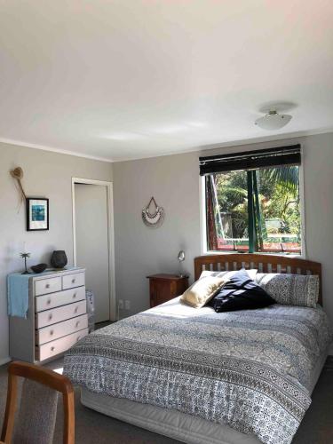 a bedroom with a bed with a dresser and a window at First Light in Mangawhai
