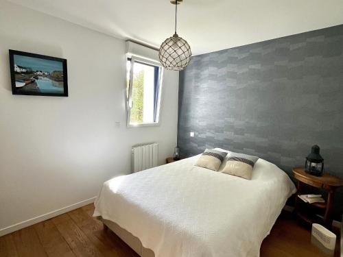 a bedroom with a white bed with a gray accent wall at Charmante maison à Groix proche du port - FR-1-813-35 in Kerlo