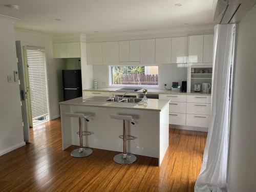 una cocina con armarios blancos y una isla con taburetes. en Allawah at Wamberal, en Wamberal