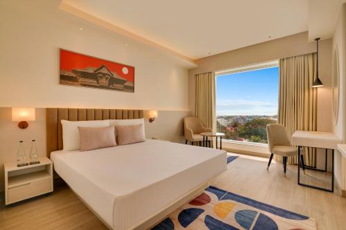 a bedroom with a bed and a desk and a window at Lemon Tree Premier, Thiruvananthapuram in Trivandrum