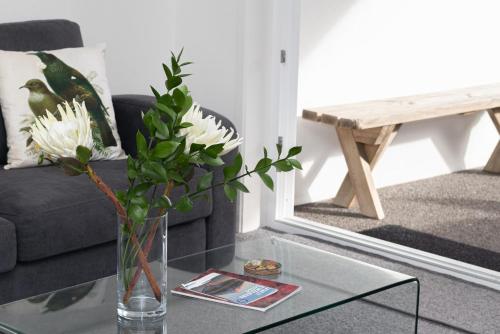 a vase with white flowers on a glass table in a living room at By The Sea On Sackville - beachside in Fitzroy in New Plymouth