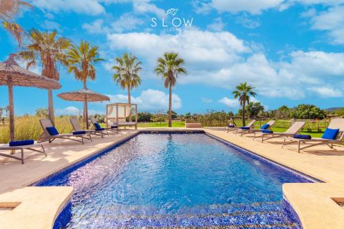 a pool with chairs and umbrellas and palm trees at Villa Es Contes by Slow Villas in Santanyi