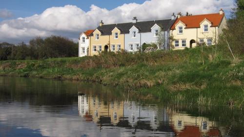 ein großes gelbes Haus auf einem Hügel neben einem Fluss in der Unterkunft Craobh Haven Cottages in Craobh Haven