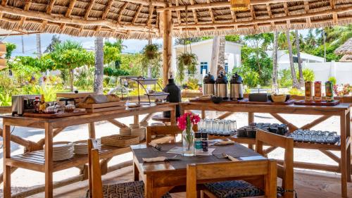 キウェンワにあるCoconut Breeze Apartmentsの木製のテーブルと椅子、テーブルと食べ物を用意したレストランを併設しています。