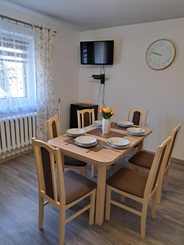une table à manger avec des chaises et une horloge murale dans l'établissement Pociechówka apartament, à Tylicz