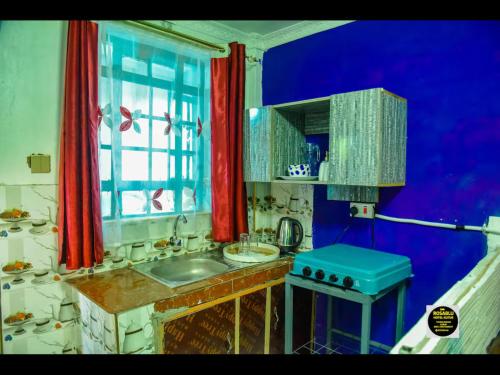 a kitchen with a sink and a window with red curtains at RosaBlu Hotel Kutus in Gakuo