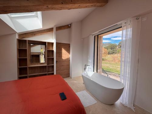 a bedroom with a bed and a tub and a window at La Master Grange De Queyran in La Palud sur Verdon