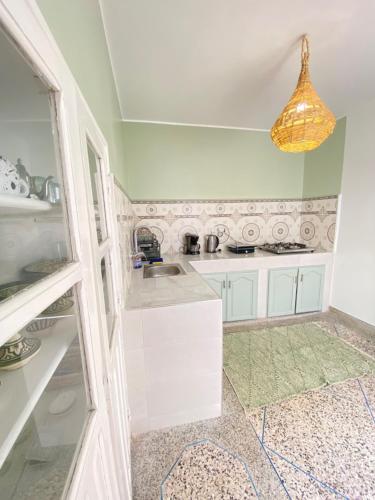 una cocina con armarios blancos y una lámpara. en Dar Minel- Deine Wohlfühloase mit Garten und Sonnenterasse, en Zaouit Massa