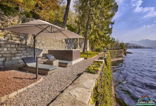 a bench with an umbrella next to a body of water at Villa Scoglio with Private Hot Tub and Air Conditioning in Lierna