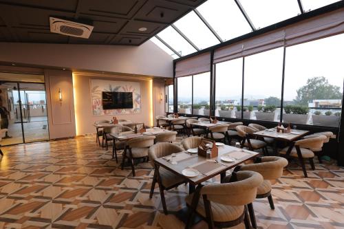 Un restaurante con mesas y sillas y grandes ventanales. en Hotel Ganga Sutra, en Dehradun
